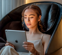 Frau liest auf einem Tablet in einem schwarzen Massagesessel