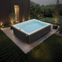 Grauer rechteckiger Outdoor-Whirlpool in einem Garten bei Dämmerung