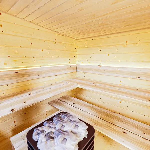 Holzverkleideter Innenraum der Gartensauna Hetki mit L-förmigen Bänken und Ofensteinen