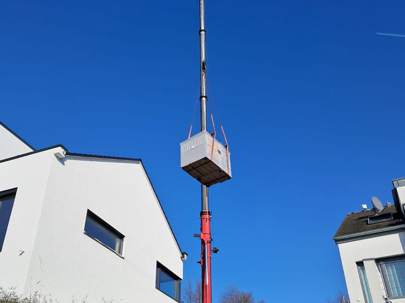 Verpackte Hetki Gartensauna wird von einem Kran zwischen zwei Wohnhäusern angehoben