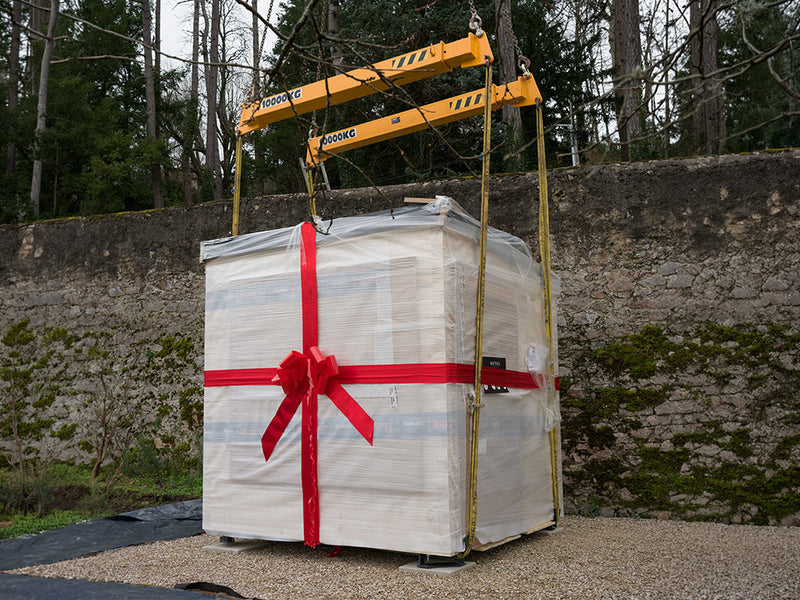 Verpackte Hetki Gartensauna mit roter Schleife unter einem Kran-Traversenrahmen