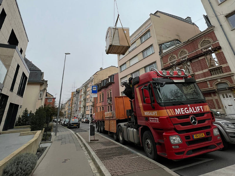 Verpackte Gartensauna wird von einem Kranwagen über eine innerstädtische Straße gehoben
