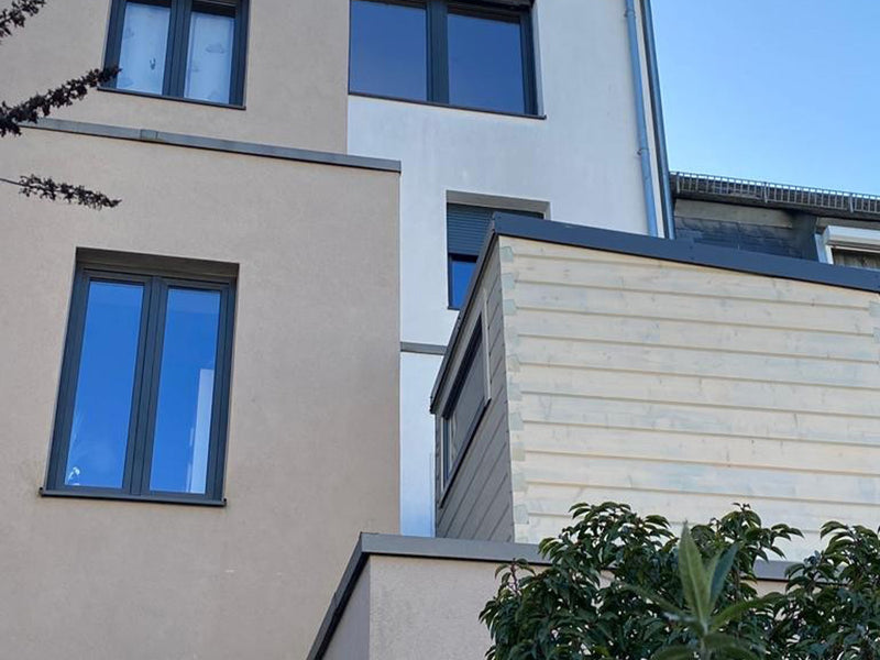 Helle Holz-Gartensauna auf einer Terrasse unmittelbar neben einem mehrstöckigen Wohnhaus