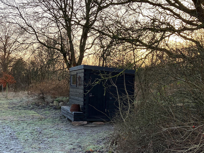 Kompakte schwarze Gartensauna in einer frostbedeckten Waldlichtung