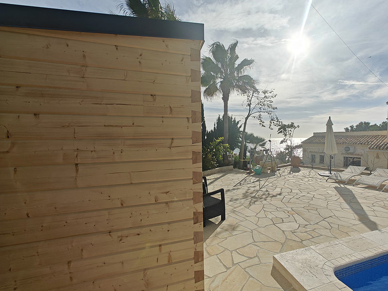 Helle Holz-Gartensauna auf einer sonnigen Poolterrasse mit Palmen