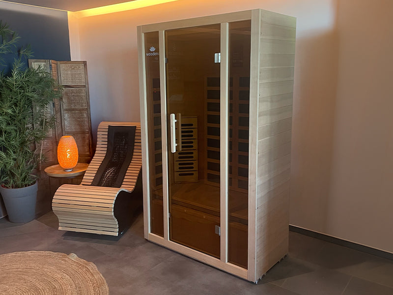 Woodena Infrarotkabine mit Glasfront neben einer Holzliege und leuchtender Tischlampe