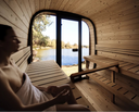 Person mit Handtuch sitzt in einer Gartensauna mit Blick auf einen See