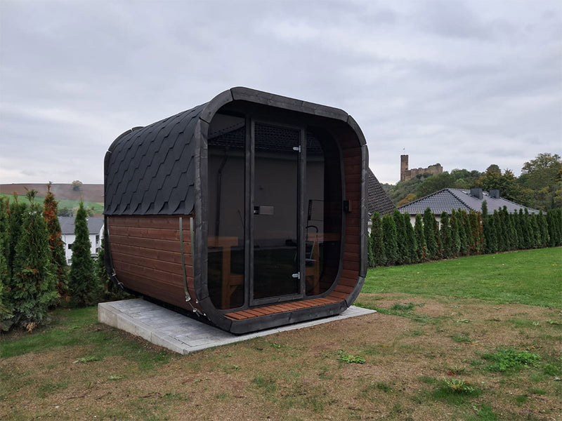 Kaunis Gartensauna mit dunklem Schindeldach, Holzseiten und Glasfront auf einer Wiese
