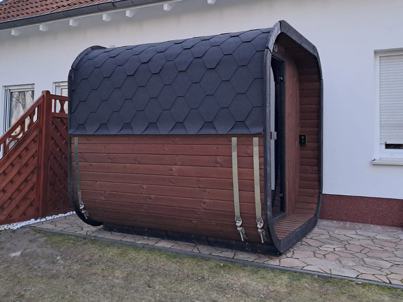 Seitenansicht einer Kaunis Gartensauna mit Holzverkleidung und dunklem Schindeldach neben einem Haus