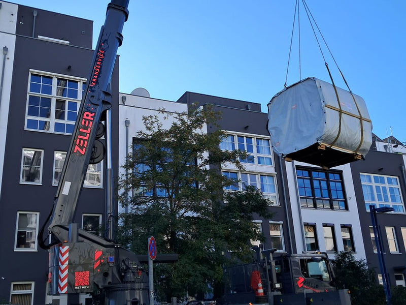 Verpackte Kaunis Gartensauna wird mit einem Kran vor einem städtischen Gebäude angehoben