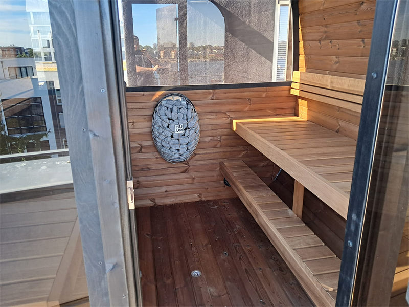 Innenraum der Kaunis Gartensauna mit Holzbank, Saunaofen und Fensterblick über die Stadt
