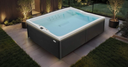 Grauer rechteckiger Outdoor-Whirlpool auf einer beleuchteten Gartenterrasse