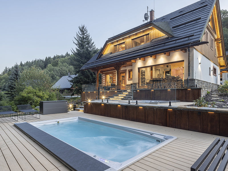 Eingelassener Swim-Spa auf einer beleuchteten Terrasse vor einem Landhaus bei Dämmerung