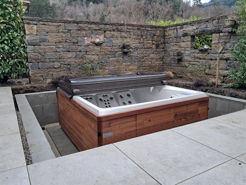 Whirlpool mit Holzverkleidung und gefalteter Abdeckung in einem von Natursteinmauern umgebenen Innenhof