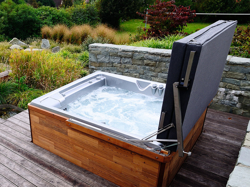 Sprudelnder Outdoor-Whirlpool mit geöffneter Abdeckung auf einer Holzterrasse im Garten