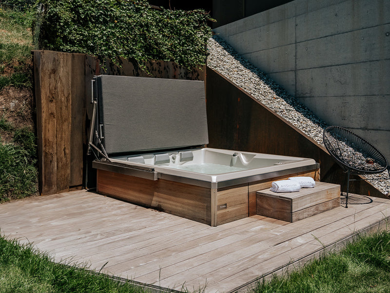 Whirlpool mit Holzverkleidung, geöffneter Abdeckung und Stufen auf einer kleinen Holzterrasse