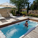 Frau im sprudelnden VIVO SPA WaterFit 3 auf einer Holzterrasse mit Liegestühlen