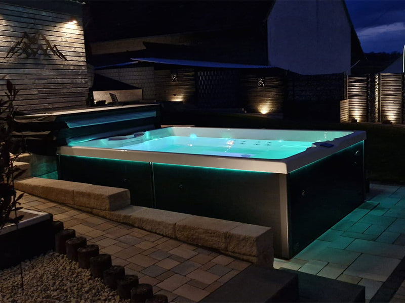 Türkis beleuchteter VIVO SPA AUREA Whirlpool auf einer Gartenterrasse bei Nacht