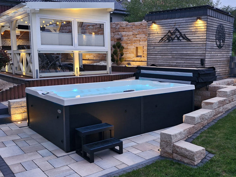 Blau beleuchteter VIVO SPA AUREA Whirlpool mit Treppe auf einer Terrassenanlage bei Dämmerung