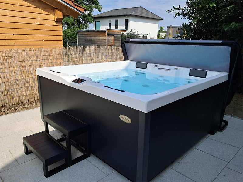 Geöffneter VIVO SPA AUREA Whirlpool mit dunkler Verkleidung und Einstiegstreppe auf einer Terrasse