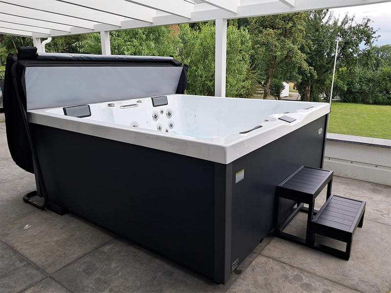 Geöffneter VIVO SPA AUREA Whirlpool mit dunkler Verkleidung und Einstiegstreppe unter einem Terrassendach
