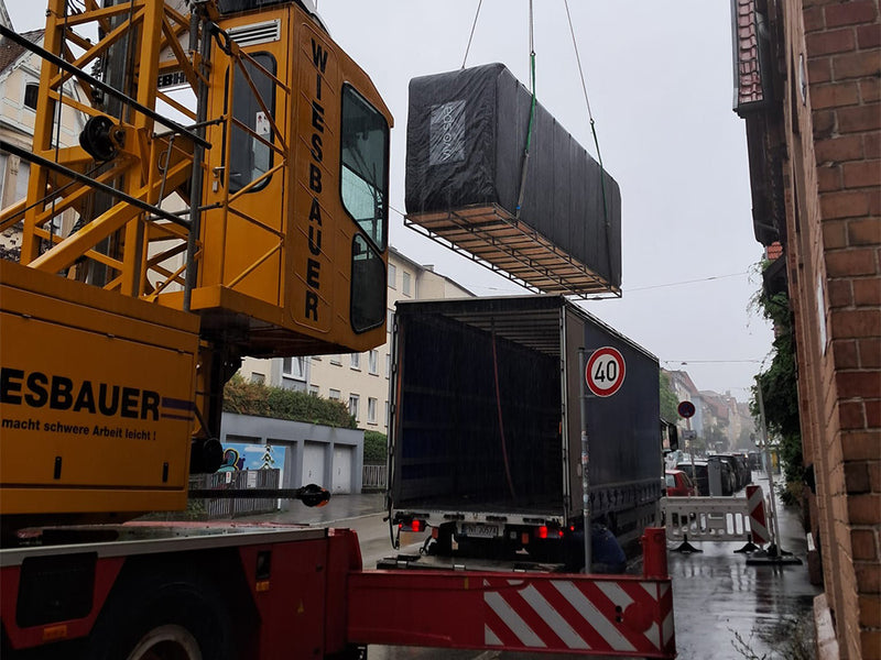 Verpackter Waterfit Swim-Spa wird auf einer regennassen Stadtstraße mit Kran aus einem Lkw gehoben