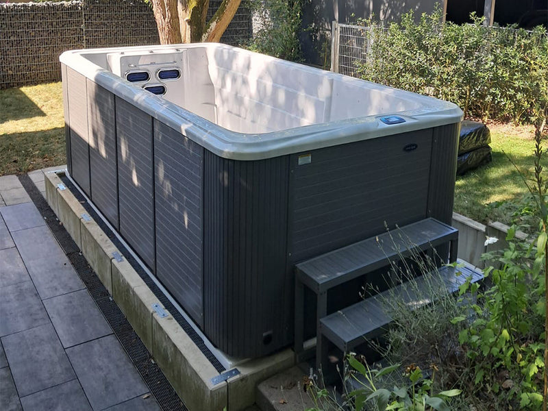 Leerer VIVO SPA Waterfit Swim-Spa mit dunkler Verkleidung und Einstiegstreppe im Garten