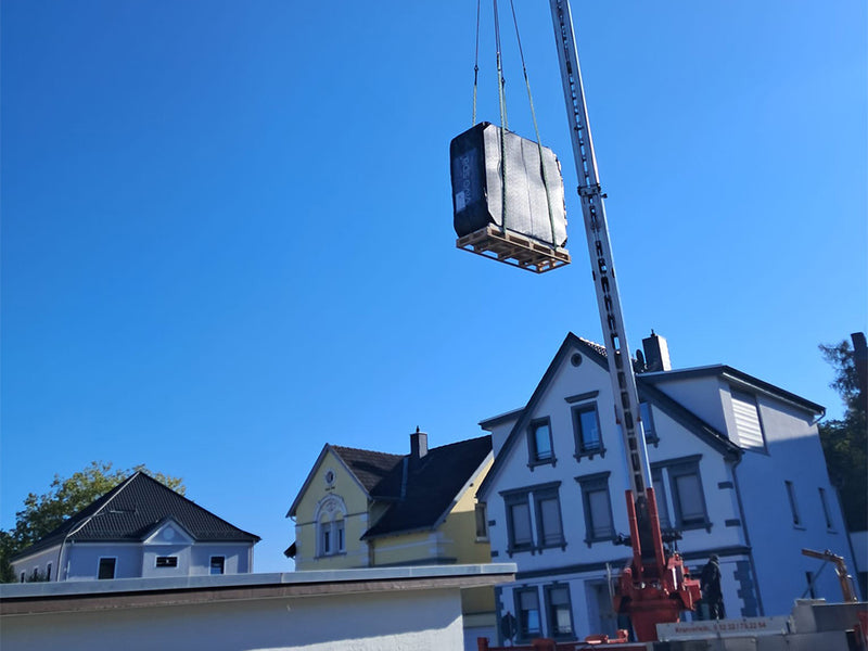Aufrecht verpackter WELUXIA Whirlpool wird mit einem Kran über Wohnhäuser gehoben