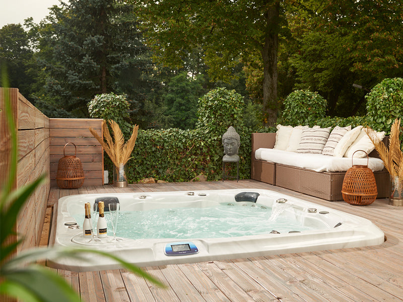 In eine Holzterrasse eingelassener WELUXIA Whirlpool mit Champagnerflaschen, Sitzgruppe und Buddhafigur