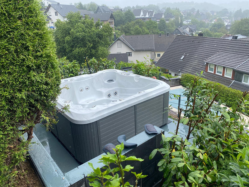 Leerer WELUXIA Whirlpool mit dunkler Verkleidung auf einem Hanggrundstück mit Blick über eine Ortschaft