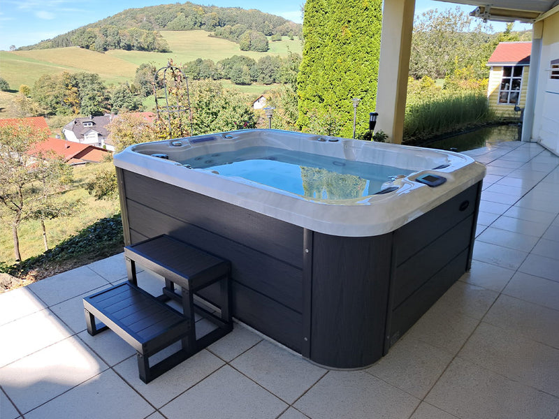 WELUXIA Whirlpool mit Einstiegstreppe auf einer überdachten Terrasse mit Blick über Hügel