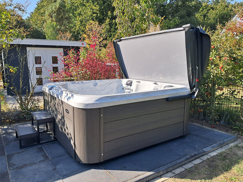 Geöffneter WELUXIA Whirlpool mit dunkler Verkleidung und Stufen in einem herbstlichen Garten