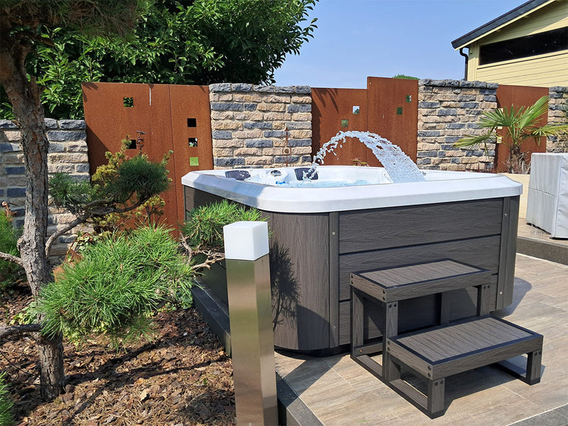 WELUXIA Whirlpool mit bogenförmigem Wasserstrahl und Einstiegstreppe auf einer Gartenterrasse
