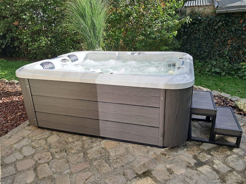 Sprudelnder WELUXIA Whirlpool mit dunkler Verkleidung und Einstiegstreppe auf einer steinernen Gartenterrasse