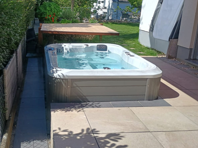 Teilweise eingelassener WELUXIA Whirlpool neben einem Wohnhaus und einer erhöhten Holzplattform