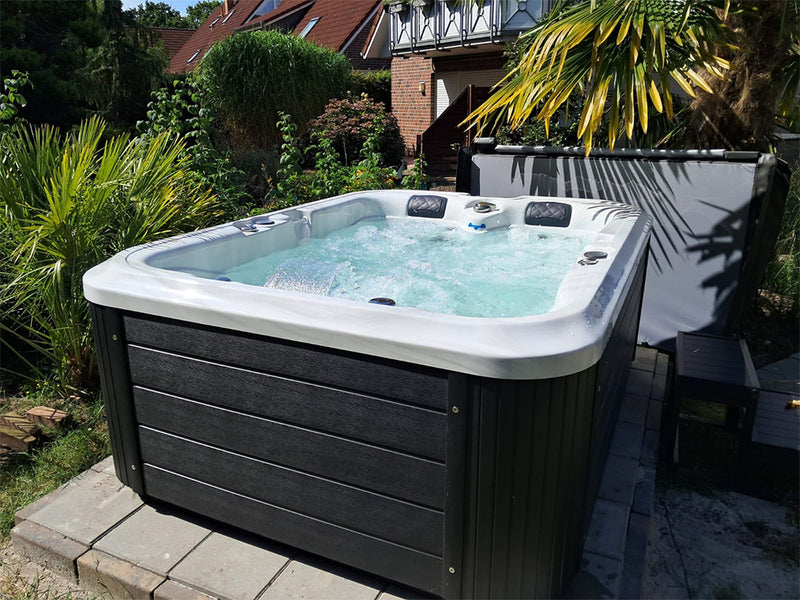 Sprudelnder WELUXIA Whirlpool mit geöffneter Abdeckung in einem Garten mit Palmen