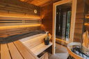 Beleuchteter Saunaraum der Round Cube Gartensauna mit Holzofen und L-förmigen Bänken