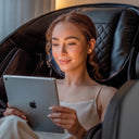 Frau sitzt mit einem Tablet in einem schwarzen Massagesessel