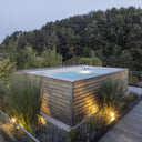 USSPA Swim Spa M mit Holzverkleidung in einem bepflanzten Garten bei Abendlicht
