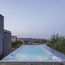 Längsansicht des beleuchteten USSPA Swim Spa M auf einer erhöhten Terrasse mit Stadtpanorama