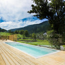 USSPA Swim Spa XL auf einer hellen Holzterrasse mit Blick auf eine grüne Berglandschaft