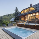 USSPA Swim Spa XL auf einer großen Holzterrasse vor einem beleuchteten Berghaus