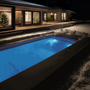 Blau beleuchteter USSPA Swim Spa XL im Schnee vor einem Haus mit Weihnachtsbaum bei Nacht