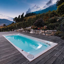 USSPA Swim Spa XL auf einer dunklen Holzterrasse vor einer bepflanzten Bergkulisse bei Abendlicht