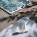 Geöffnetes Buch und Getränk neben dem sprudelnden VIVO SPA AUREA 6 Whirlpool