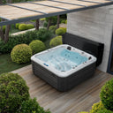 Sprudelnder Outdoor-Whirlpool mit dunkler Verkleidung unter einer Pergola im Garten