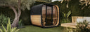 Gartensauna mit Holzverkleidung und schwarzem Schindeldach zwischen üppigen Pflanzen