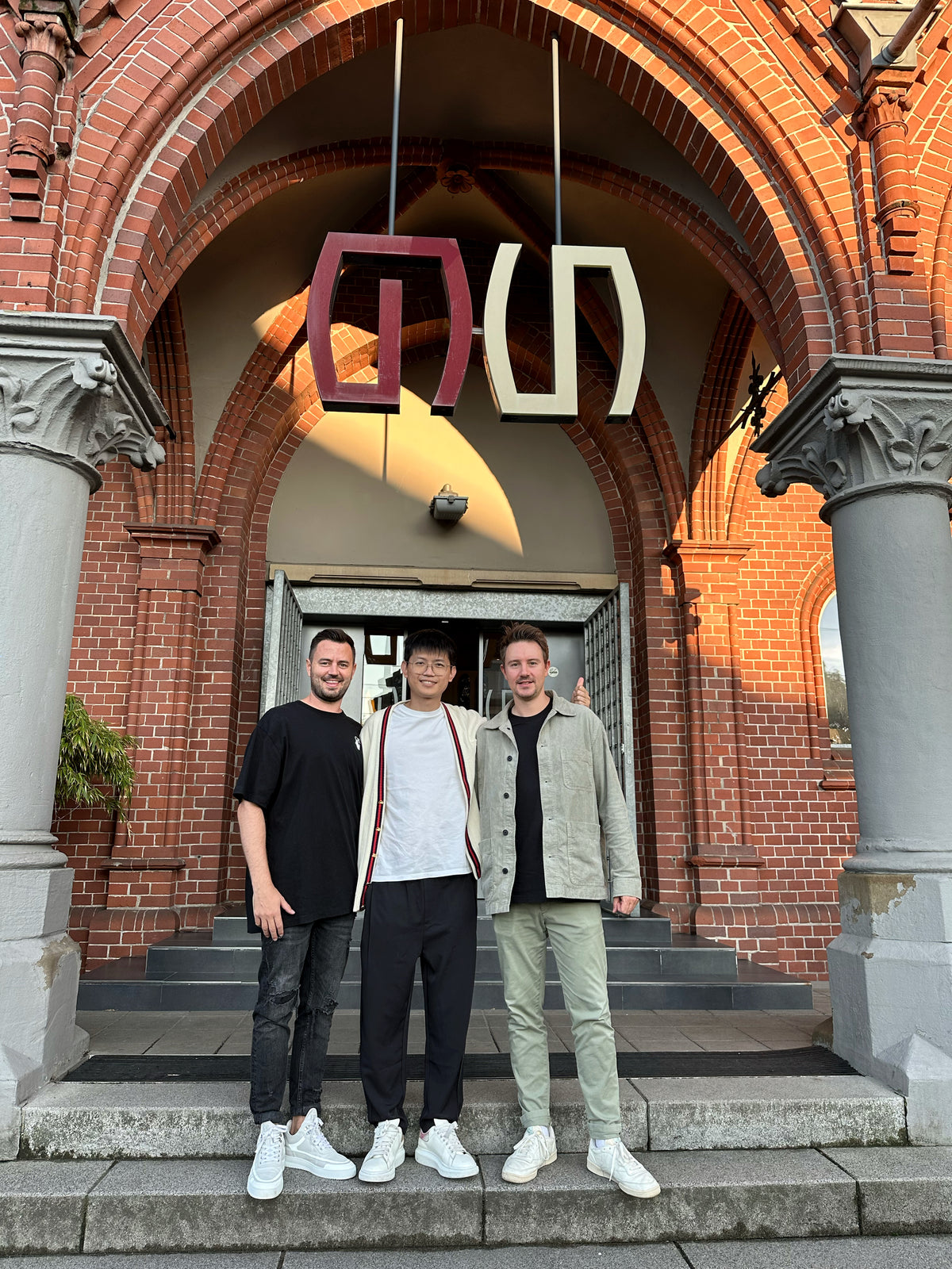 Dennis Buck und Florian Öttking mit einem langjährigen Partner und guten Freund vor einem Backsteingebäude