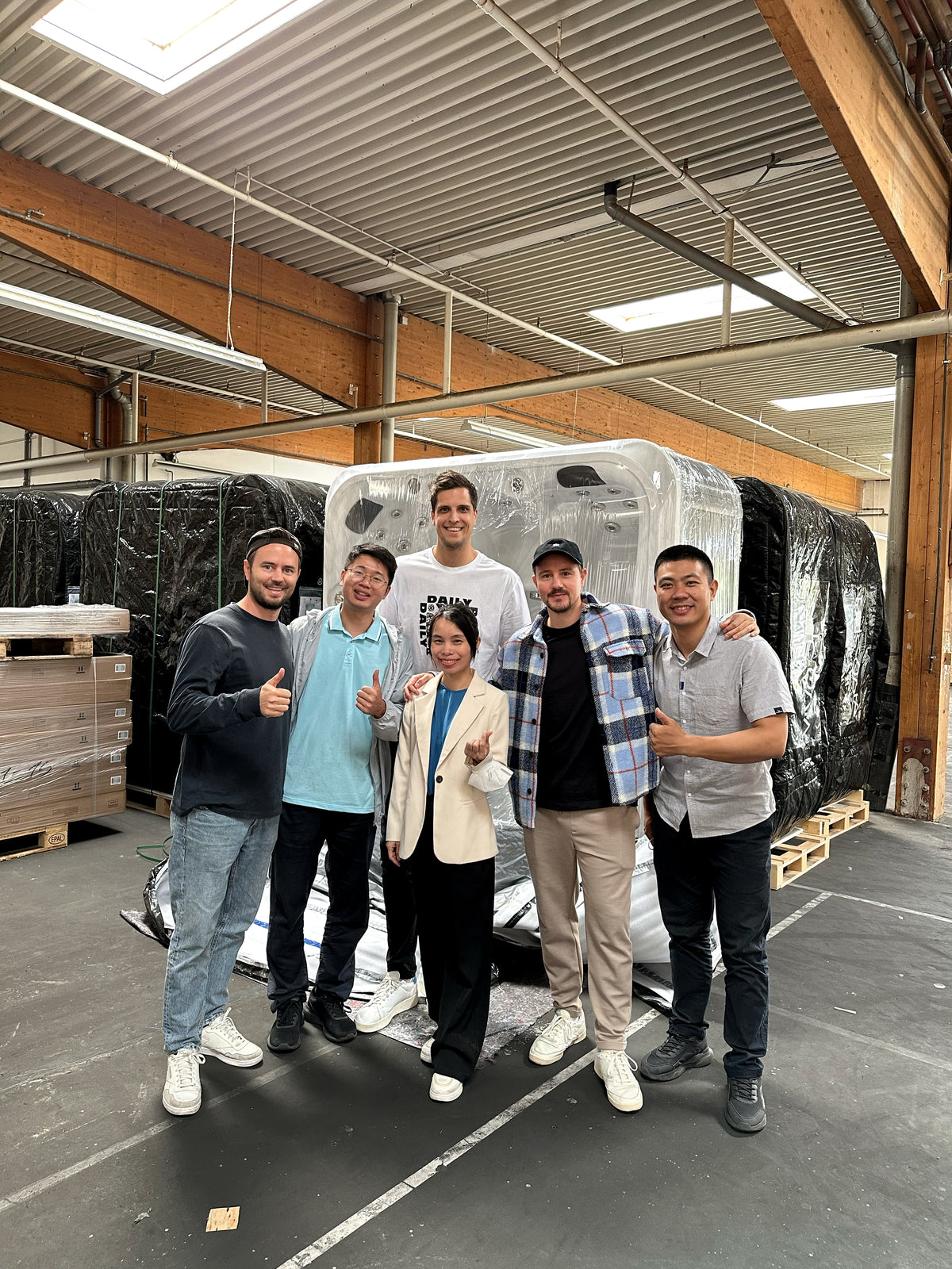 Sechs Personen bei einem Partnerbesuch vor verpackten Whirlpools in einer Lagerhalle
