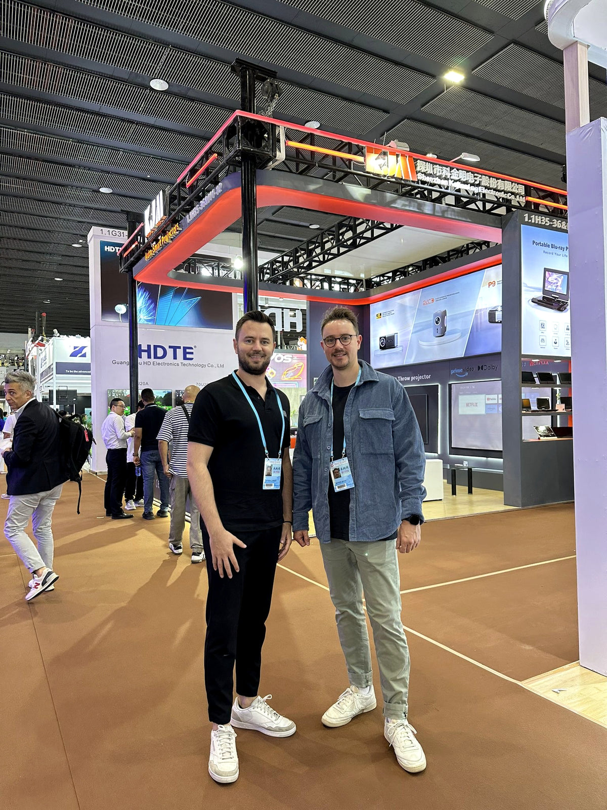 Zwei Besucher auf einer internationalen Messe vor einem Stand für Elektronikprodukte